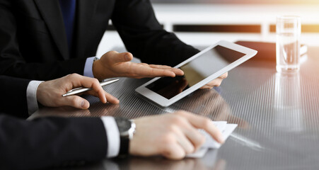 Businessman using tablet computer and work together with his colleague in sunny modern office, close-up. Unknown business people at meeting. Teamwork and partnership concept