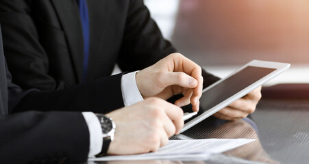 Businessman using tablet computer and work together with his colleague in sunny modern office, close-up. Unknown business people at meeting. Teamwork and partnership concept