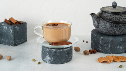 Masala tea chai in a glass cup with traditional teapot on podium or pedestal. Traditional Indian...