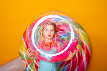 Funny little girl in swimming suit with swimming inflatable ring smiling having fun on yellow background.