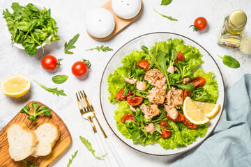 Green Salad with baked salmon. Green salad mix with tomatoes and salmon. Top view at white table.