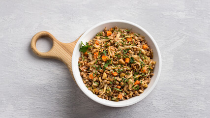 Delicious vegetarian buckwheat with cabbage, carrots, onions, nuts and herbs on a light gray textured background, top view. Homemade diet healthy food	