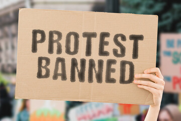 The phrase " Protest banned " on a banner in men's hand with blurred background. Rally. Riot. Violation. Illegal. Government. Movement. Control. Protesting