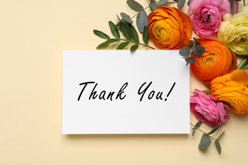 Beautiful ranunculus flowers and greeting card with text Thank You on beige background, flat lay