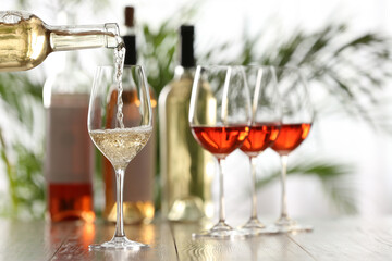Pouring white wine from bottle into glass on wooden table, space for text