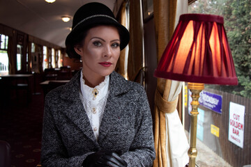 Portrait of beautiful female in 1920s costume with cloche hat sitting in vintage train carriage...