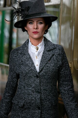 Beautiful english woman dressed in 1920s costume walking on railway platform with train in...