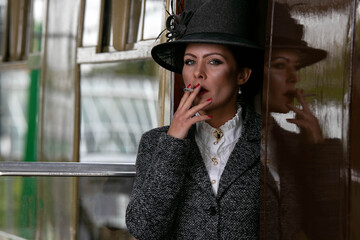 Beautiful female in vintage 1920s costume smoking cigarette while leaving train at train station