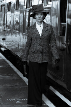 Beautiful english woman dressed in 1920s costume walking on railway platform with train in background
