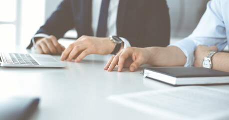 Unknown business people using laptop computer at the desk in modern office. Businessman or male entrepreneur is working with his colleague. Teamwork and partnership concept