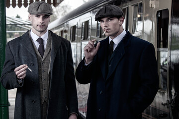 Handsome English gangsters smoking at railway station with train in the background