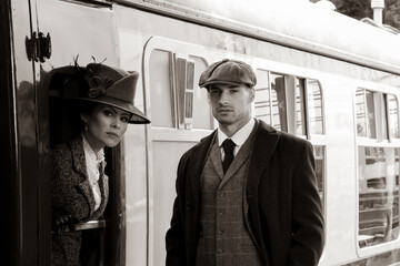 Beautiful woman dressed in vintage 1920s costume arriving by train and greeted by her bodyguard - obrazy, fototapety, plakaty