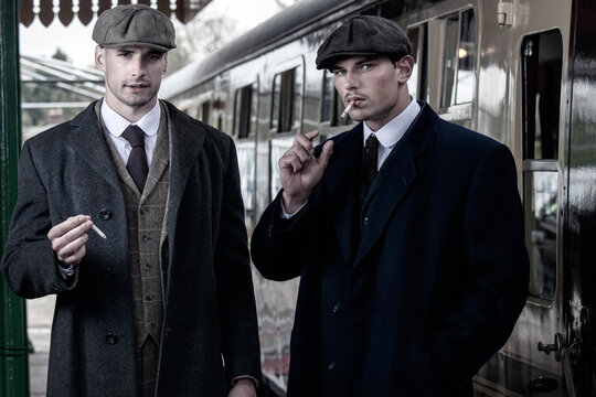 Handsome English gangsters smoking at railway station with train in the background