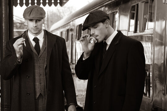 Handsome English gangsters smoking at railway station with train in the background