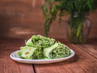 Green lavash rolls with curd cheese, cucumbers and dill on a white plate