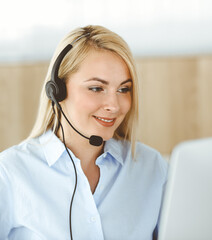 Blonde business woman sitting and communicated by headset in call center office. Concept of...