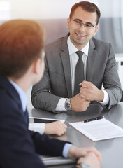 Businessman headshot at meeting in modern office. Entrepreneur sitting at the table with colleagues. Teamwork and partnership concept. Grey blazer suits to happy smiling manager