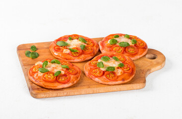 Small open pies pizzas with beet juice added to the dough, with cherry tomatoes, mozzarella and basil on a wooden board on a white background