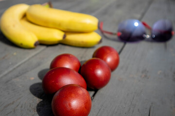 Mix composition with painted easter eggs, bunch of ripe bananas and sunglasses lying on an old wooden surface