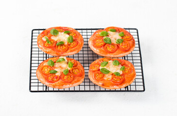 Children mini-pizzas pink with beet juice added to the dough, small open pies with tomatoes, mozzarella and basil on a serving rack on a white background