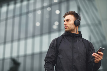 Attractive man listening to music via smartphone and headphones in urban environment