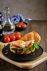 Sandwich croissant with scrambled eggs, tomatoes, cheese and greens on a black plate on a wooden table