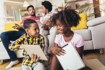 African american boy and girl lying on floor and using digital tablet. Family at home.