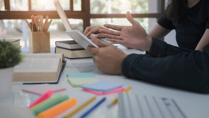 High school or college using laptop while sitting at table. Group students studying and reading with books in library. Students helps friend catching up and learning tutoring. education concepts