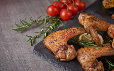 Roasted chicken wings in barbecue sauce with pepper seeds Rosemary, salt in a black stone plate on a gray stone table. top view with copy space. tasty snack for beer on a dark background. Flat lay.