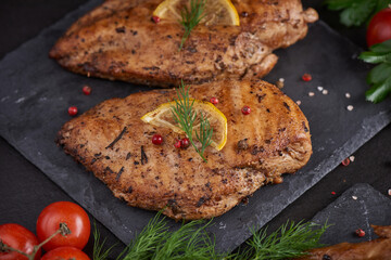 Grilled chicken breast on a stone board with tomatoes, herbs, lemon, dill, cut lemon on plate. Healthy lunch menu. Diet food. Top view.