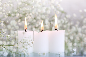 Burning candles and white flowers gypsophila on table with space for text.