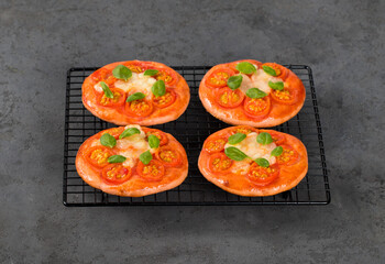 Small open pies, children mini pizzas pink with beet juice added to the dough, with cherry tomatoes, mozzarella and basil on a dark gray background