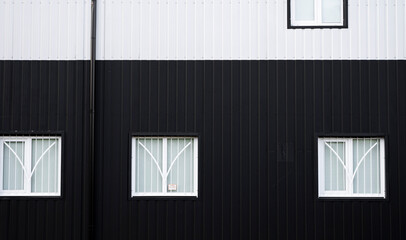 Black and white corrugated iron sheet used as a facade of a warehouse or factory with a windows. Texture of a seamless corrugated zinc sheet metal aluminum facade. Architecture. Metal texture.