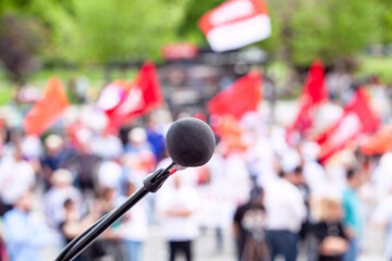 Political protest or public demonstration, focus on microphone, blurred crowd of people holding flags in the background