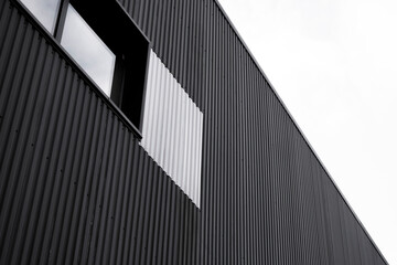 Black and white corrugated iron sheet used as a facade of a warehouse or factory with a windows. Texture of a seamless corrugated zinc sheet metal aluminum facade. Architecture. Metal texture. - obrazy, fototapety, plakaty