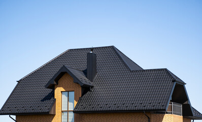 Brown corrugated metal profile roof installed on a modern house with a attic windows. The roof of...