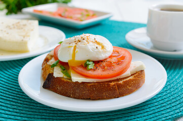 Sandwich with whole grain bread, goat cheese, fresh tomatoes and poached egg. Delicious simple breakfast. Proper nutrition