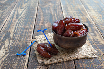 Dried dates fruit in ceramic bowl on old wooden table. Highly valuable food product.
