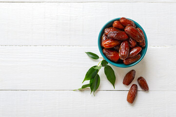 Organic sun dried dates in ceramic bowl on a white wooden background. Useful products, dried fruits. The top view. Flat lay, copy space