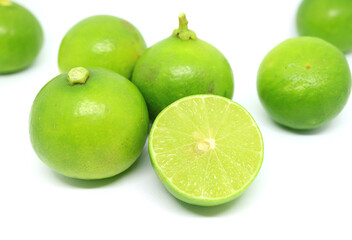 Closeup half cut vibrant green fresh lime with the whole fruits scattered on white backdrop