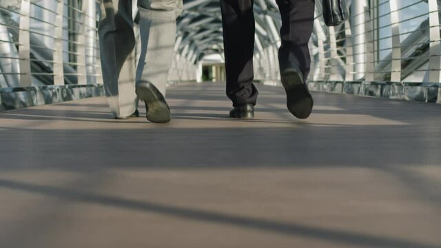 Low-section slowmo of unrecognizable businessmen legs walking along indoor glass walkway of modern high-class office building