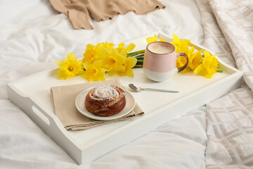 Bouquet of beautiful daffodils, bun and coffee on bed