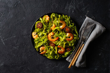 Green pasta with shrimp, basil and tomato on black background, top view, copy space, flat lay