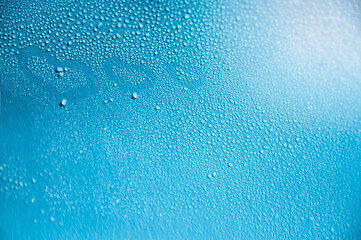 Blue background with water drops and drawn 3 hearts on wet glass with selective focus and highlights in the upper corner of the photo.