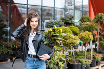A young pretty girl, dressed in a leather jacket and jeans, stands near the flower center and holds...