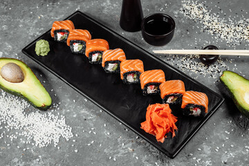 A set of sushi rolls Philadelphia with red fish, cream cheese and black rise lies in a plate boat. Sushi rolls on a gray background