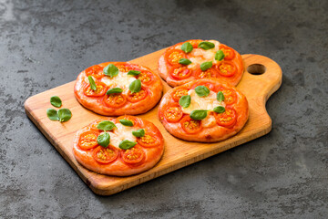 Children mini pizza pink with beet juice added to the dough, small open pies with cherry tomatoes, mozzarella and basil on a dark background