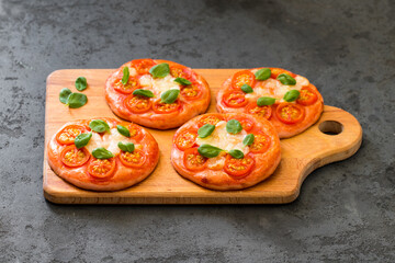 Mini pizza pink with beet juice added to the dough, small open pies with cherry tomatoes, mozzarella and basil on a wooden board on a dark background