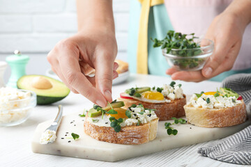 Woman putting microgreen onto sandwich at table, closeup