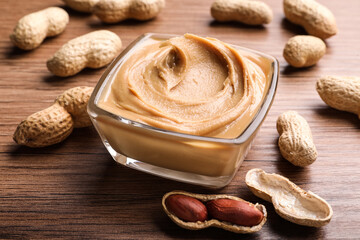 Yummy peanut butter in glass bowl on wooden table, closeup